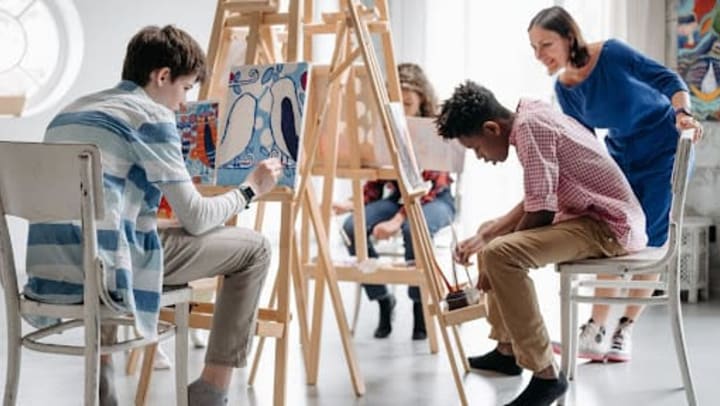 Three people painting while sitting down in front of easels with instructor watching