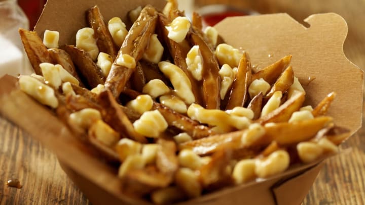 An order of classic poutine, including french fries, cheese curds, and gravy, in a cardboard container