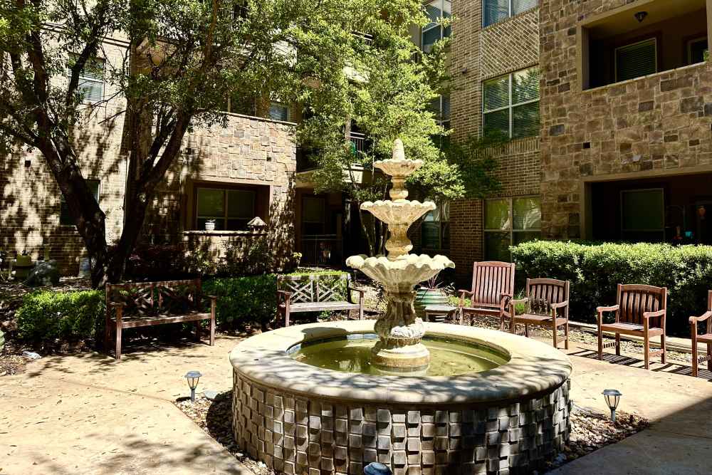 Elegant outdoor fountain surrounded by lush green bushes and outdoor seating