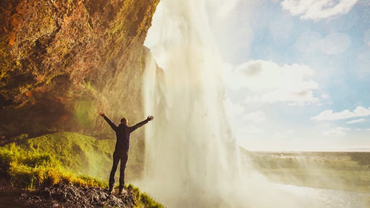 Person standing in front of a waterfall with their arms raised taking it all in