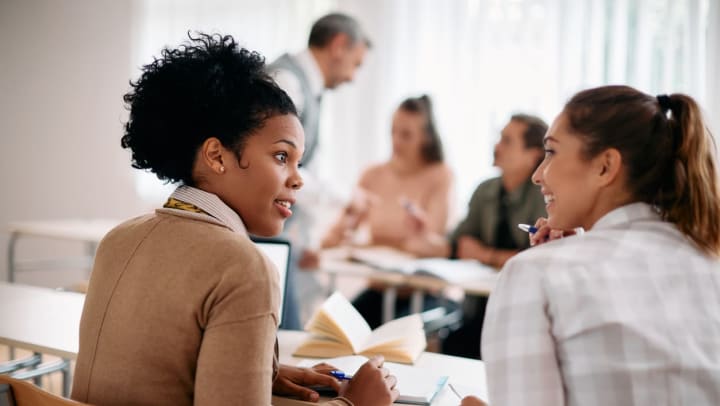 Two women communicating while learning during a class in a classroom. | Universities in Meridian