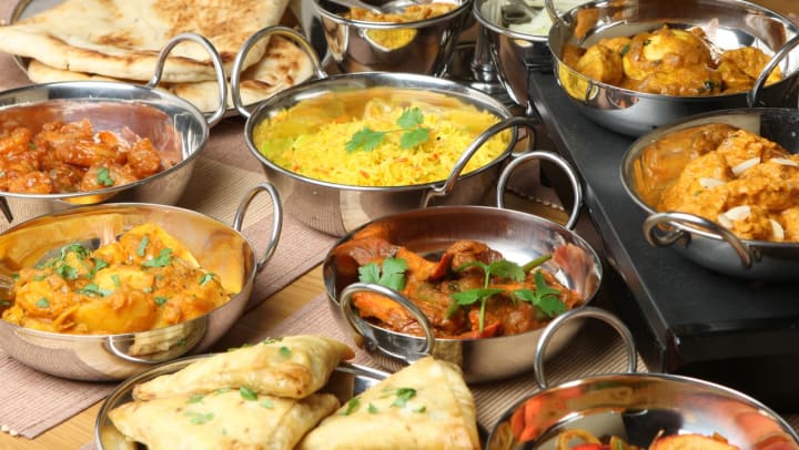 a close-up of a variety of classic Indian food dishes in metal bowls with big handles on a wood table | indian restaurants near Savannah