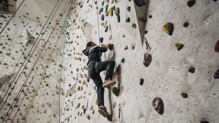 Below view of a male climbing up an indoor rock wall | rock climbing gym in Jacksonville