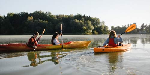 Residents joyfully navigate kayaks across a tranquil lake near Bayside Villas Apartment Homes in South Pasadena, Florida