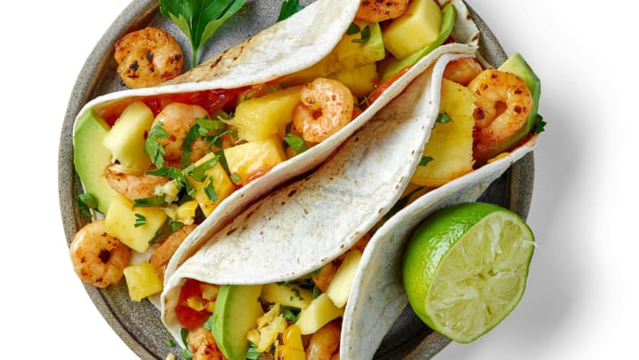 Two flour tortillas stuffed with shrimp, pineapple and avocado with half lime on the side. 