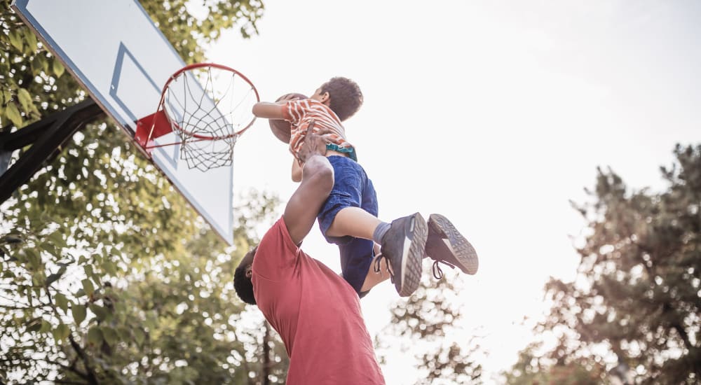A father lifting his child to a basketball net at Clinton Towne Center Apartments in Clinton, Utah