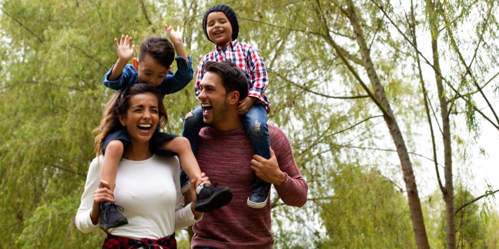 Two parents walking through a park with kids on their shoulders near Mission University Pines in Durham, North Carolina