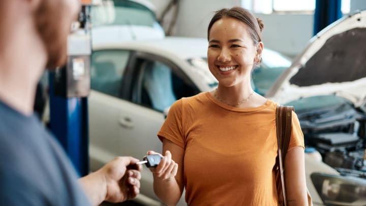 Woman at a car repair shop handing over car key to mechanic