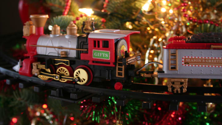 A model train on a track in front of a decorated holiday tree.