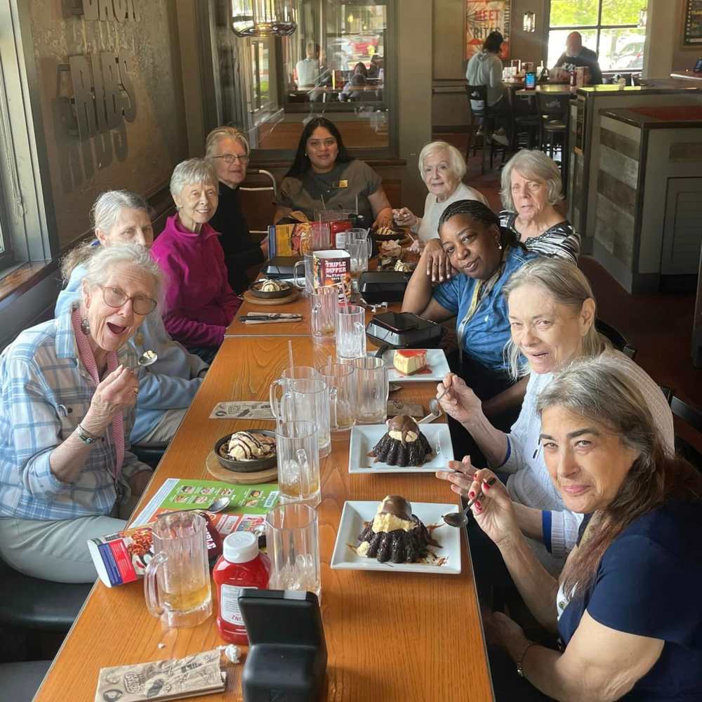 Residents and caregivers sharing laughter and desserts during a group dining outing from Watermere Frisco memory care.