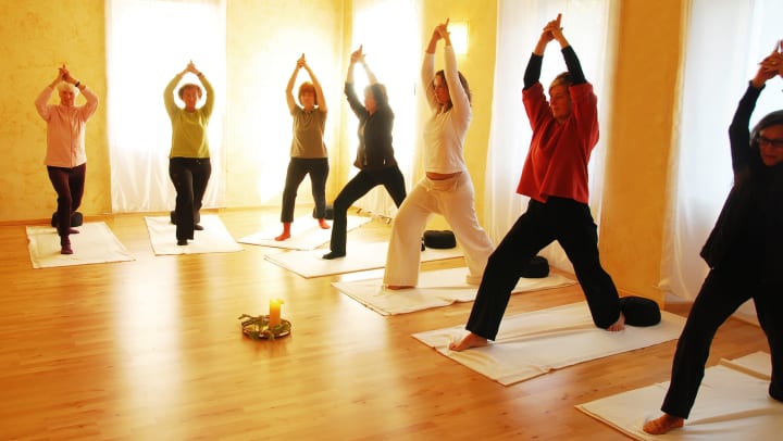 A group of women in a yellow room all stand on mats and reach upward in a yoga pose | Jacksonville’s yoga studios