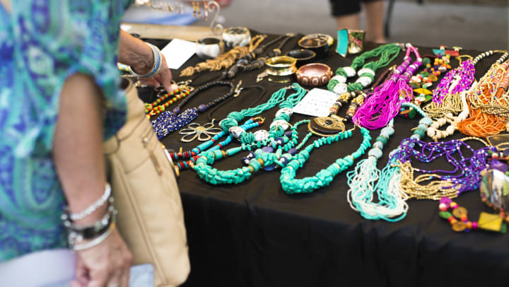 A woman looking at a variety of colorful necklaces on a table