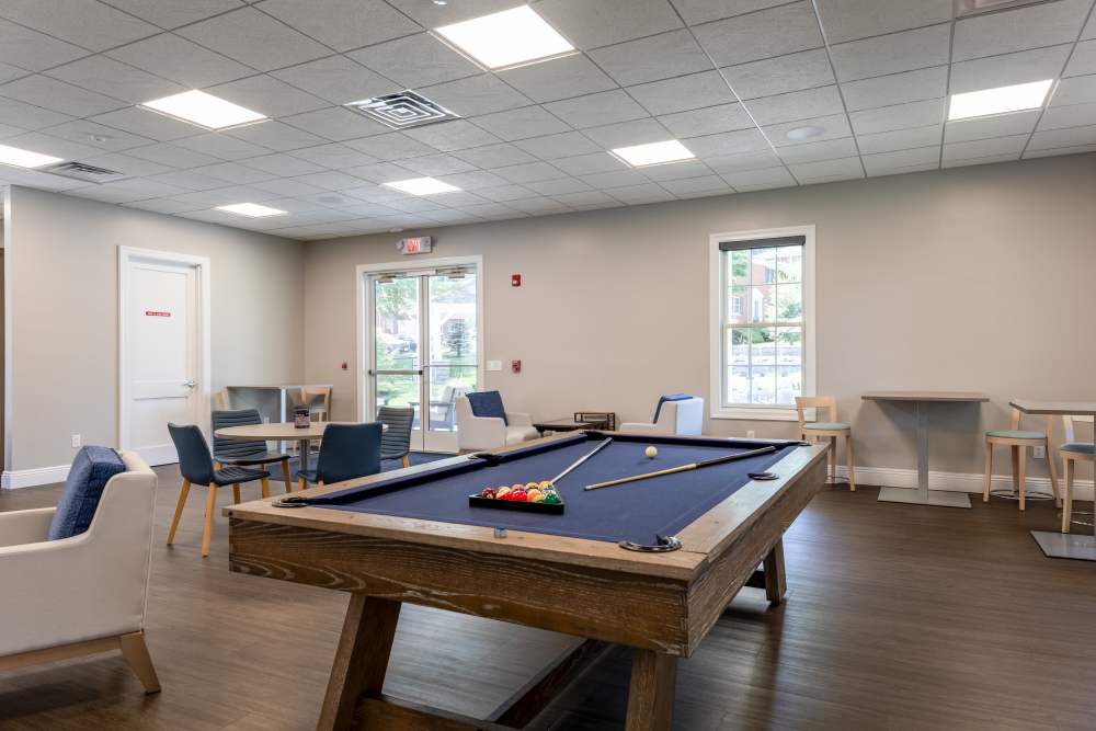Game room with a pool table, surrounding chairs and tables, large windows, and wood‑look flooring at Center Grove Village in Randolph, New Jersey.