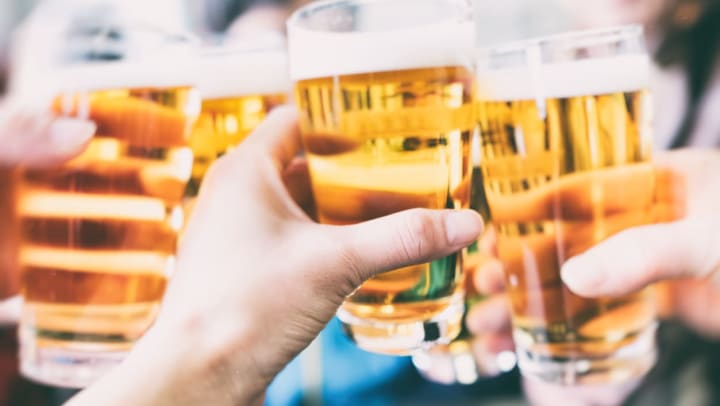  A closeup of four hands bringing together glasses of golden-colored beer in a toast