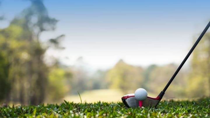 Close up of a golf club head lining up behind a golf ball on a tee