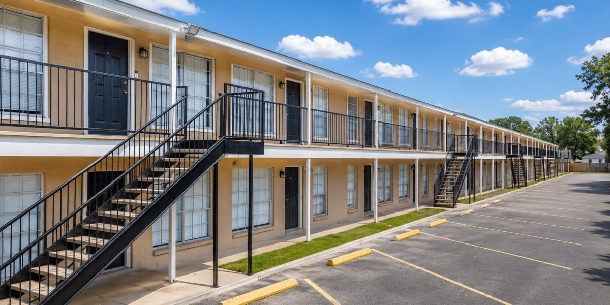 Two-story apartment community with exterior staircases and parking spaces under a sunny sky at Pecan Villas Apartments in Houston, Texas 