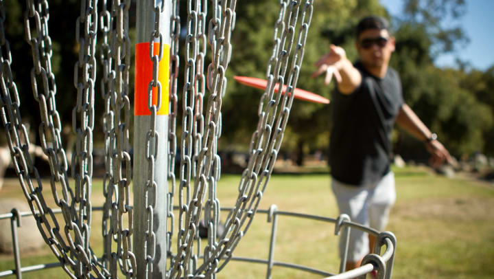 Man tossing a disc at the goal for disc golf 