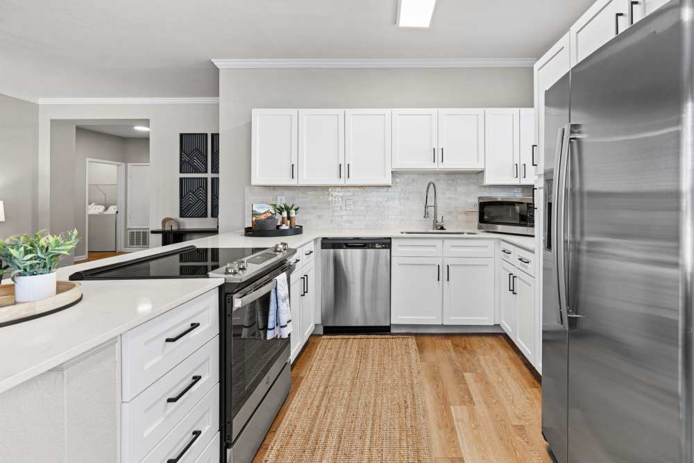 Kitchen with white cabinets, stone counters, stainless steel appliances &amp; wood-style flooring.