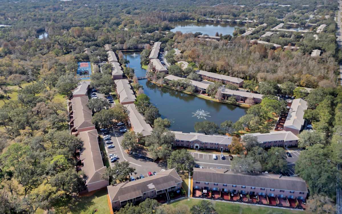Aerial view of apartment community with scenic pond, surrounded by landscaped greenery and parking areas at Carlton Arms North in Tampa, Florida