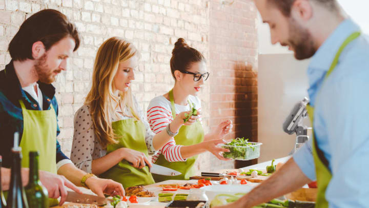 Four people participating in a cooking glass while wearing green aprons | Cooking Schools Around Albuquerque