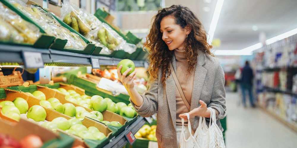 Woman selecting green apple in a grocery store, surrounded by fresh produce and vibrant colors at The Mezzanine at Freedom in Charlotte, North Carolina