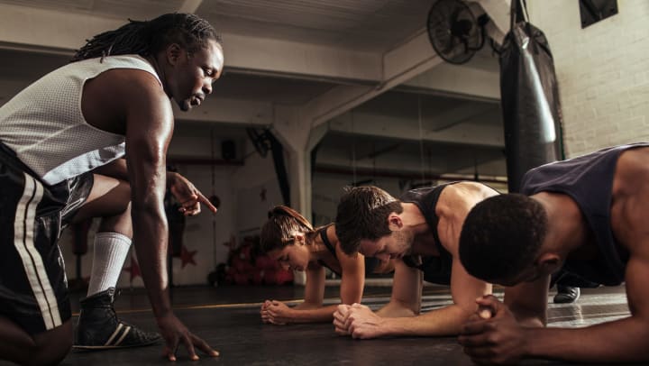 Shot of athletic people planking during a training class in the gym, with a trainer coaching them.