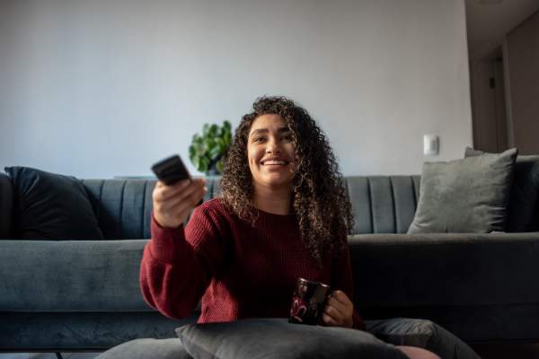 Resident woman using a remote to on the TV in an apartment at Huntersville Commons in Huntersville, North Carolina
