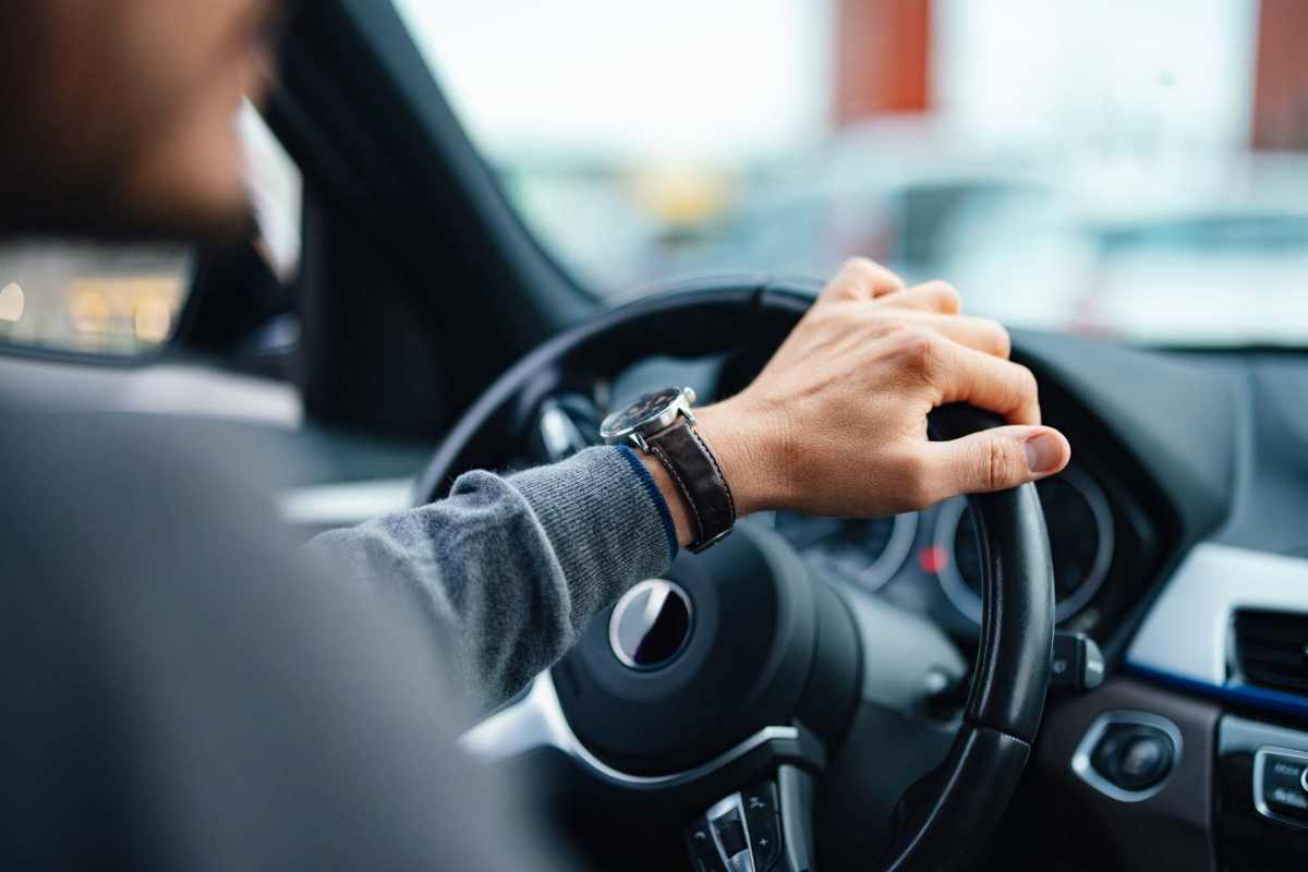 A man driving a car with his hand on the steering wheel at Granite Creek in Rocklin, California.
