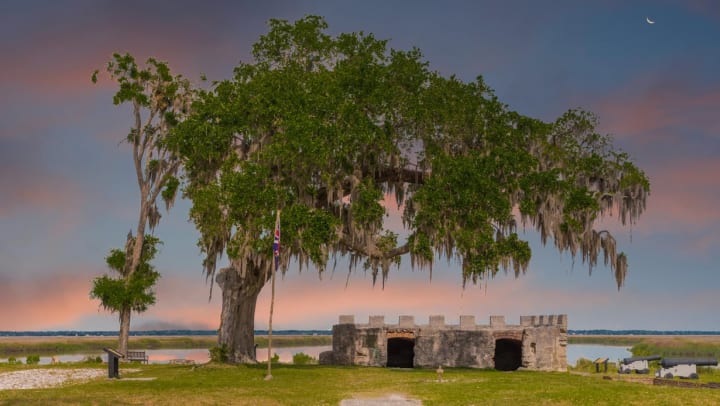 The crumbled stone remnants of Fort Frederica sitting underneath a large tree at sunset 