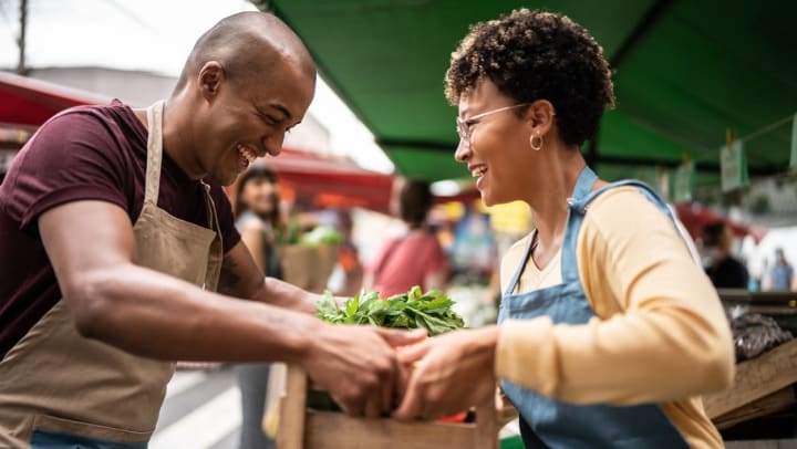 A male and female passing a wooden box full of produce to each other at a farmers market in Santa Fe