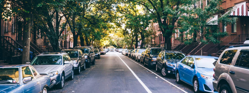 Pretty photo of a street lined with cars and covered with tons of shade from the huge trees near Eastgold NYC in New York, New York