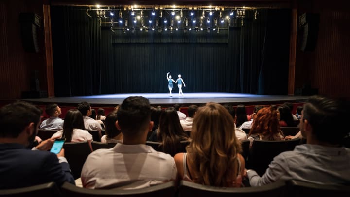 Two dancers holding hands on a stage with a full audience watching