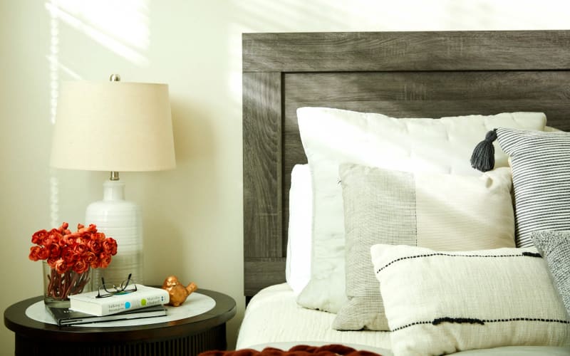 Bedside table with potted flowers, a lamp, and a book sitting on it at Amira Choice Forest Lake in Forest Lake, Minnesota