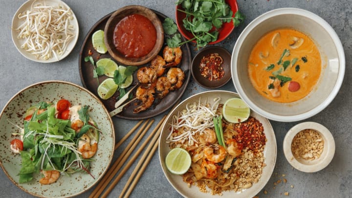 Thai dishes including pad thai, shrimp satay, and Tom Yum soup on a concrete table | Thai restaurants in Nashville