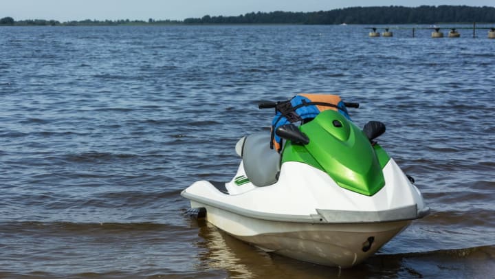 Green and white jet ski sitting on the shore of the water