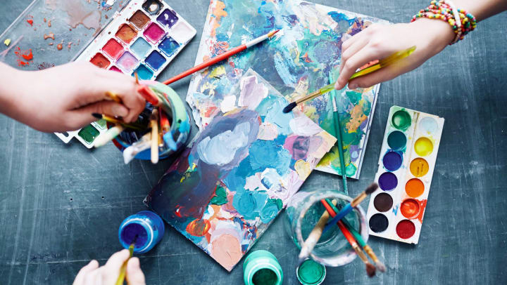 Hands holding paint brushes reach onto a surface that