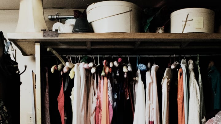 inside of a walk in closet, with clothes hanging and organizer boxes on the shelf above