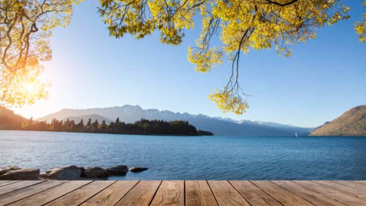 A wooden deck overlooks a calm lake, framed by stunning mountains under a clear blue sky near Auburn Hills, Michigan.