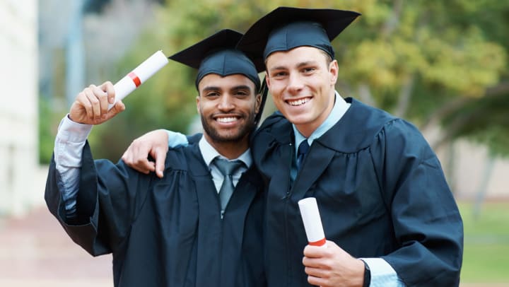 Two young men in caps and gowns posing with arms around each other.