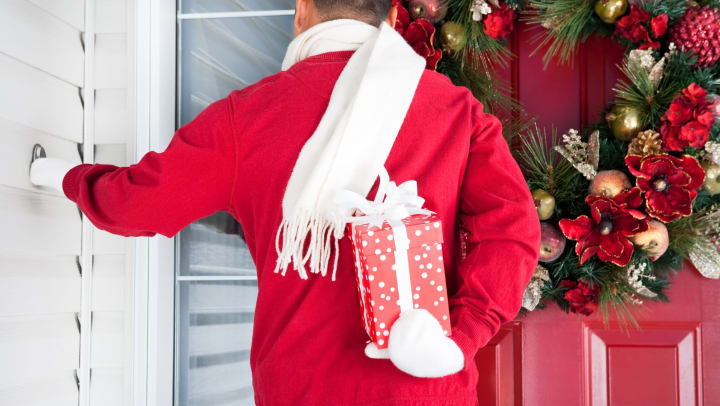Man holding a wrapped gift behind his back knocking on a decorated door