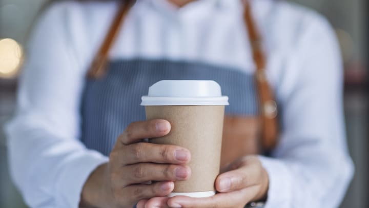 Barista holding out a cup of to go coffee