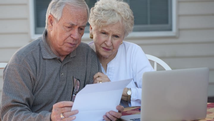 Older man and woman looking at a laptop and documents with concerned expressions