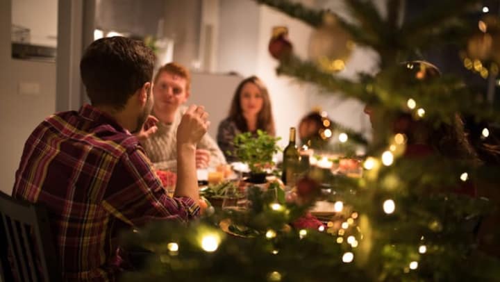  Friends eating a holiday dinner at the table near a Christmas tree