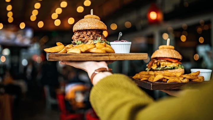 Delicious burgers and french fries are carried on a plate by a server bringing them to a patron’s table | best burgers in Katy