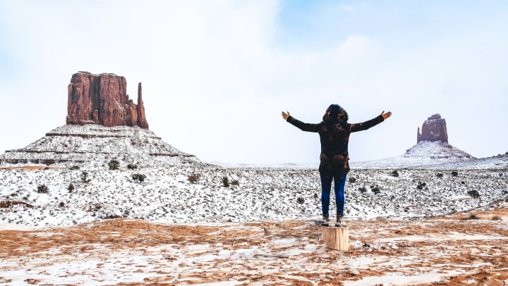 A woman standing on a tree stump in a dusting of fresh snow in Monument Valley