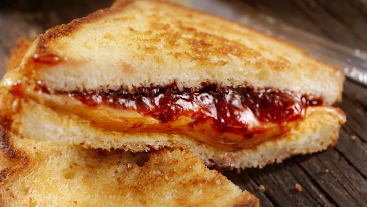 Toasted peanut butter and jelly sandwich sliced in half with one half sitting atop the other and the filling oozing out.