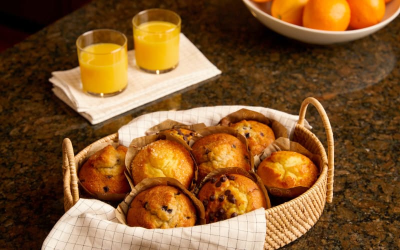 Basket of muffins next to a couple glasses of orange juice on a counter at Amira Choice Naples in Naples, Florida