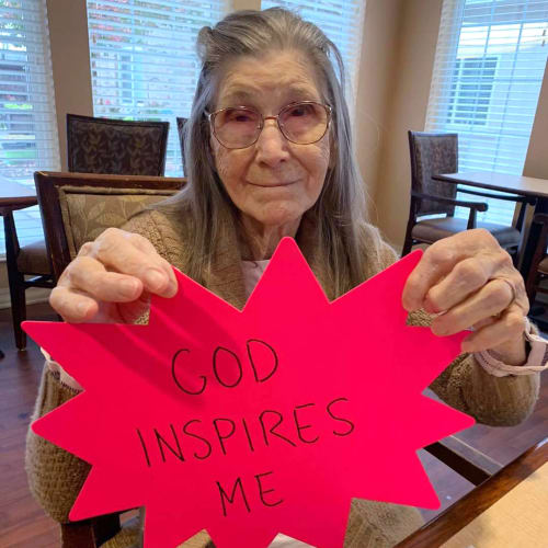 Smiling residents with piece of paper depicting the text 'God inspires me' at Oxford Glen Memory Care at Sachse in Sachse, Texas