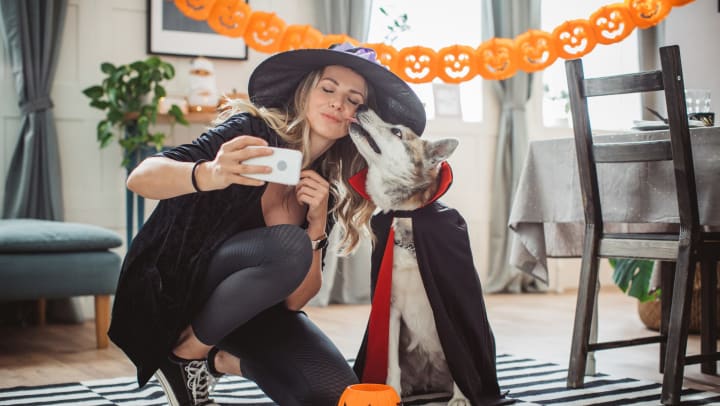 Woman dressed as a witch taking a selfie with her dog dressed as a vampire at Olympus Las Colinas