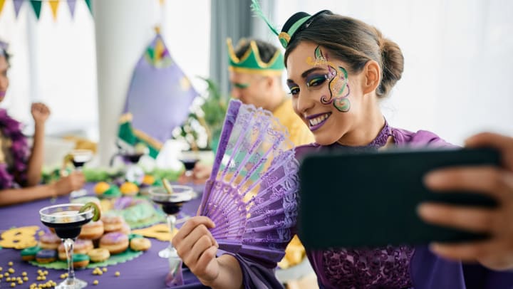 Woman wearing costume and taking selfie with cellphone at Mardi Gras party